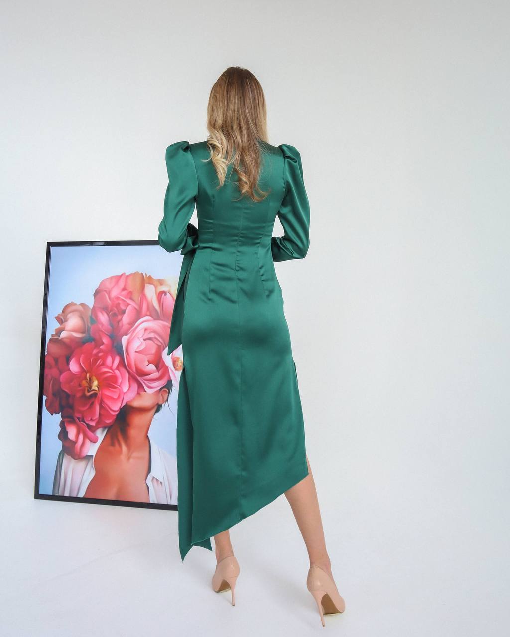 Woman wearing a green dress standing in front of a painting with pink flowers.