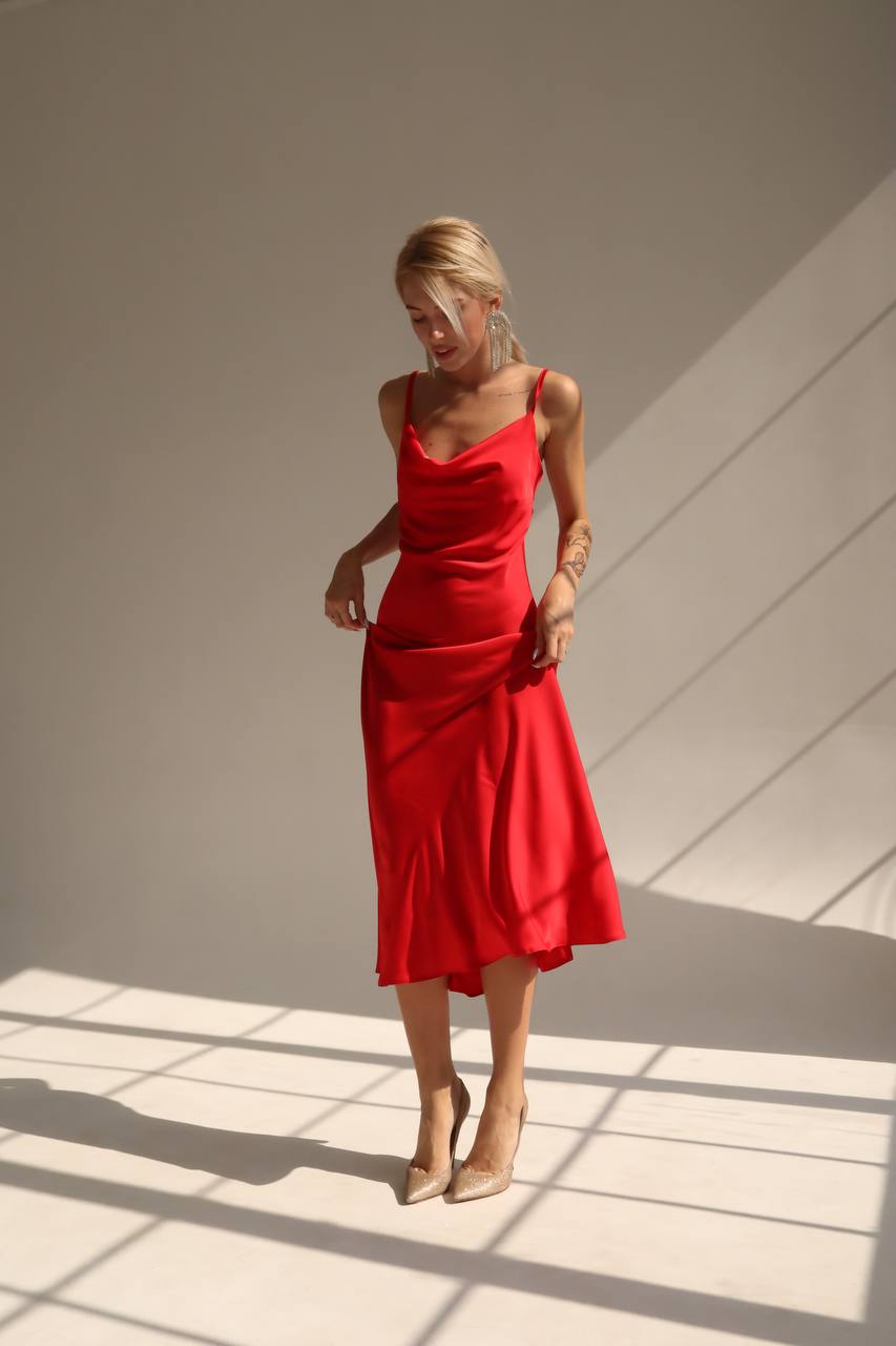 Woman wearing a red dress standing in a room with sunlight casting shadows on the wall.
