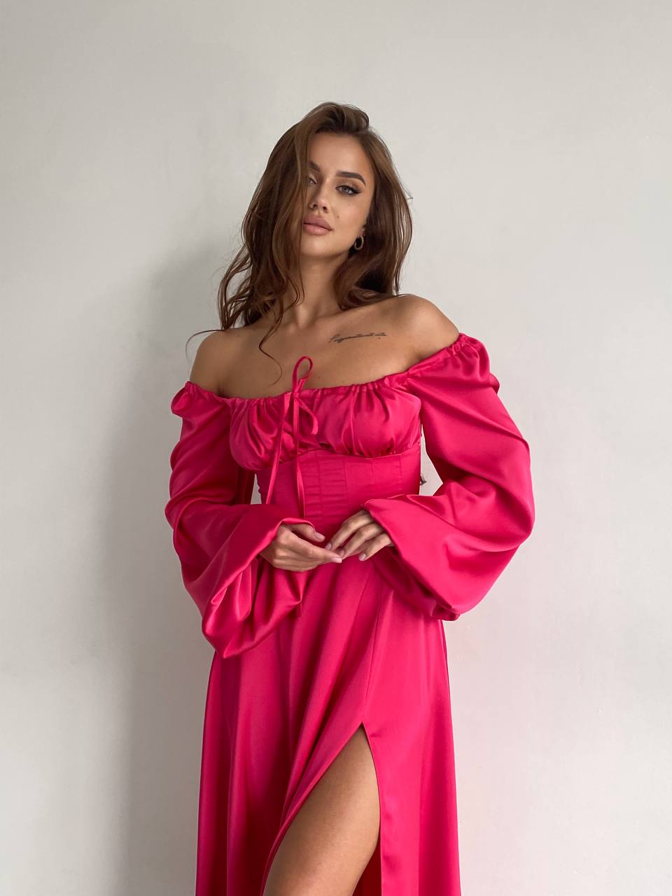 Woman wearing a bright pink off-shoulder dress with long sleeves on a plain background