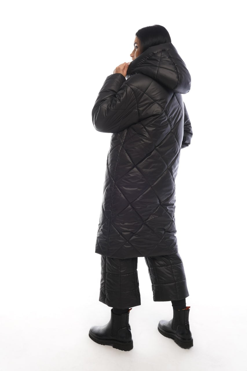 Person wearing a long black quilted coat on a white background