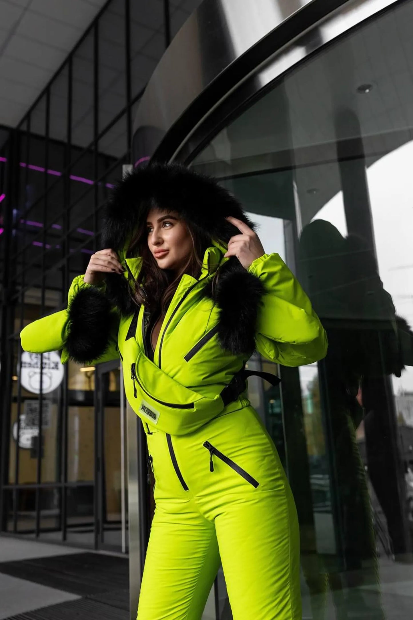 Person wearing a bright yellow snowsuit standing in front of a modern building entrance.