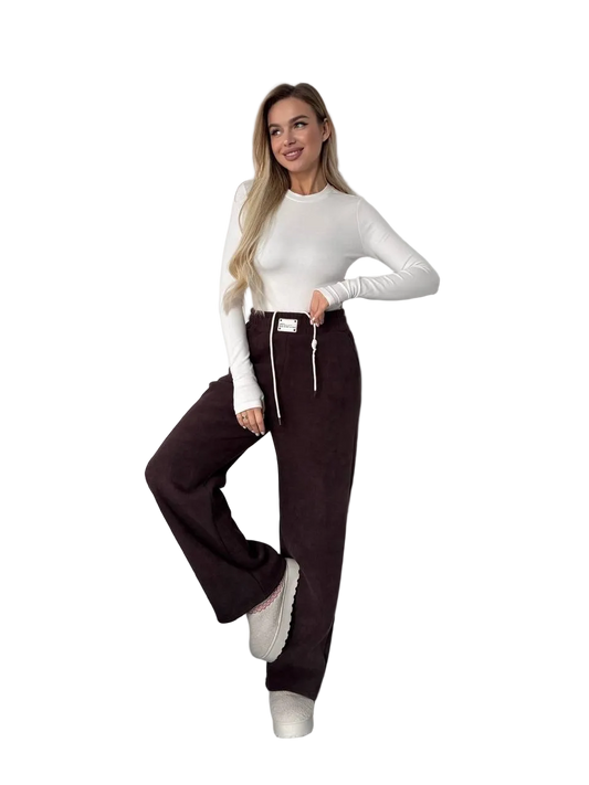 Woman wearing a white long-sleeve top and dark brown pants on a white background