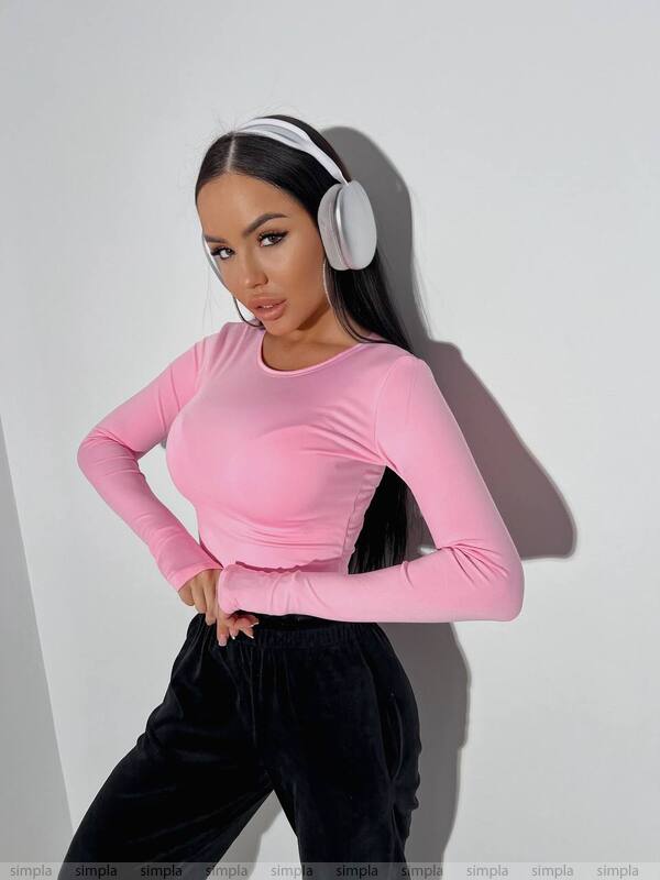 Person wearing a pink long-sleeve top and black pants with white headphones on a plain background