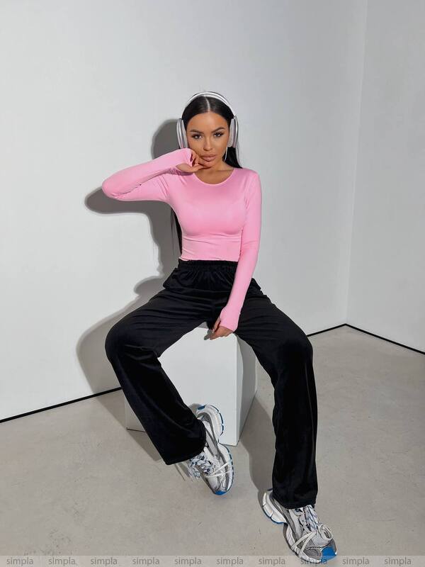Person wearing a pink long-sleeve top and black pants sitting on a white box against a plain background.