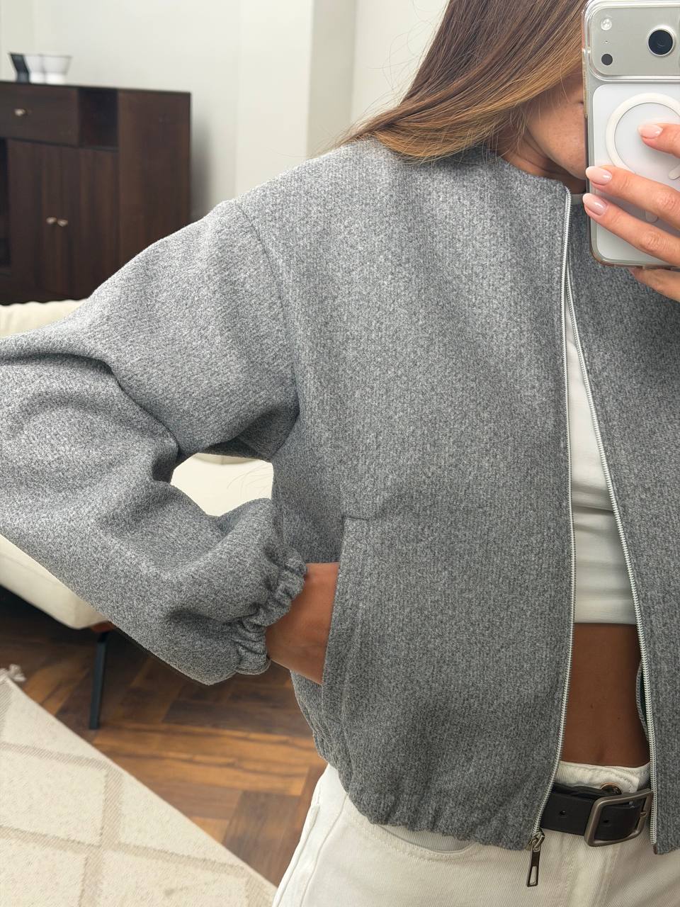 A person wearing a heather gray zip-up jacket with elasticized cuffs and a relaxed fit, photographed in a mirror selfie inside a home setting.