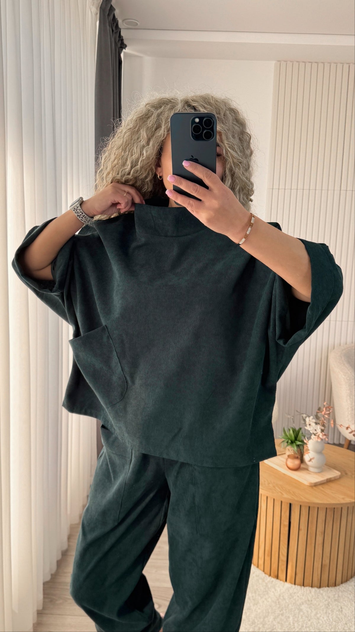 A person taking a mirror selfie in a room, wearing a dark forest green two-piece lounge set consisting of a wide-sleeve top and matching pants.