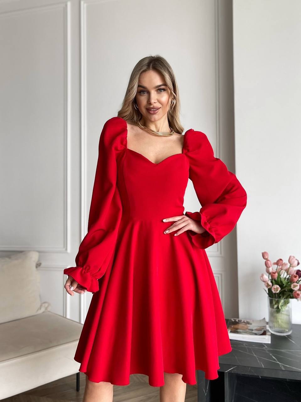 Woman wearing a red dress with puffed sleeves in an indoor setting.