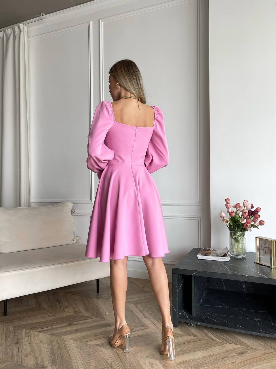 Woman wearing a pink dress in a room with a sofa and flowers.