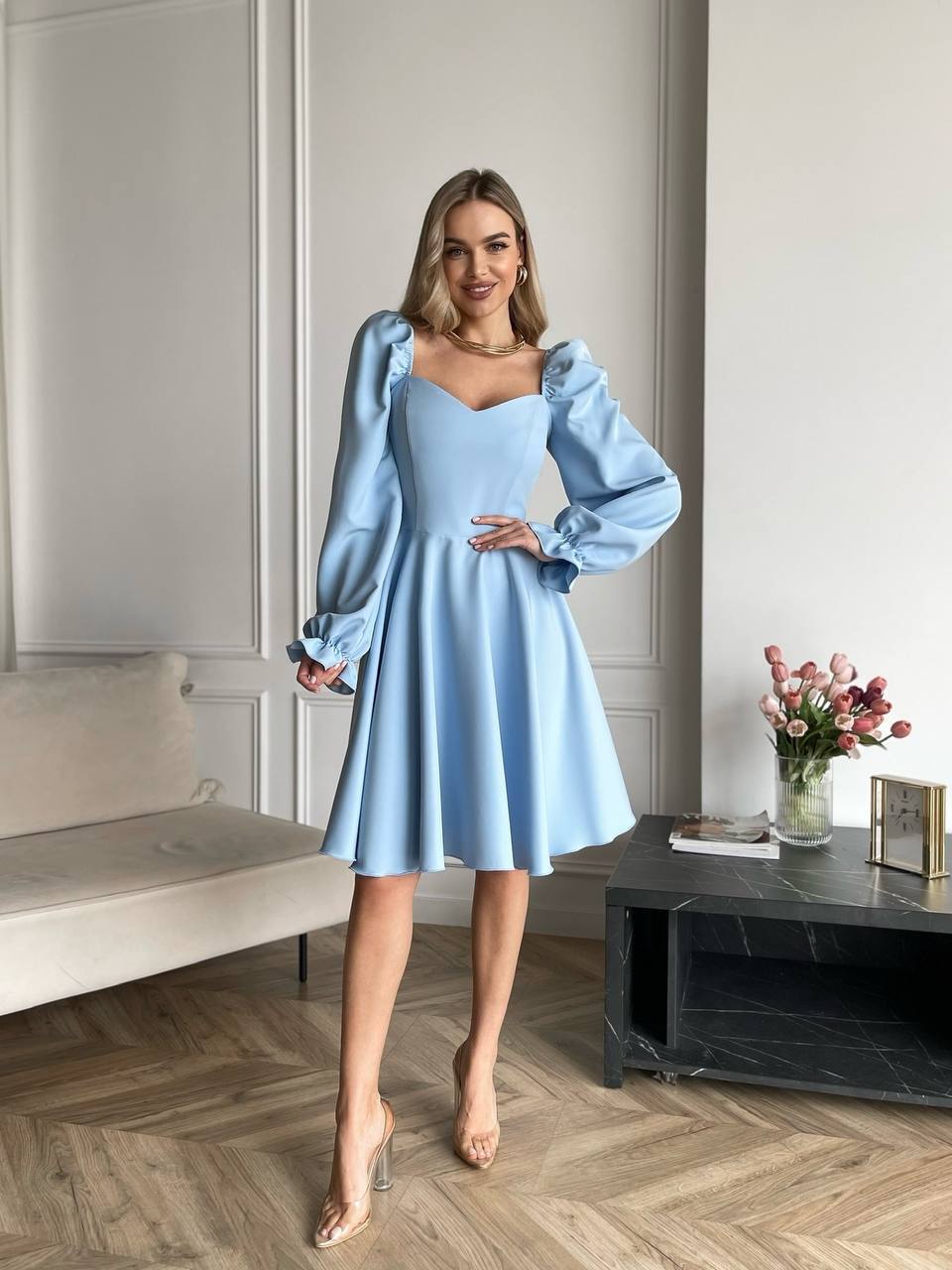 Woman in a light blue dress standing in a modern living room.