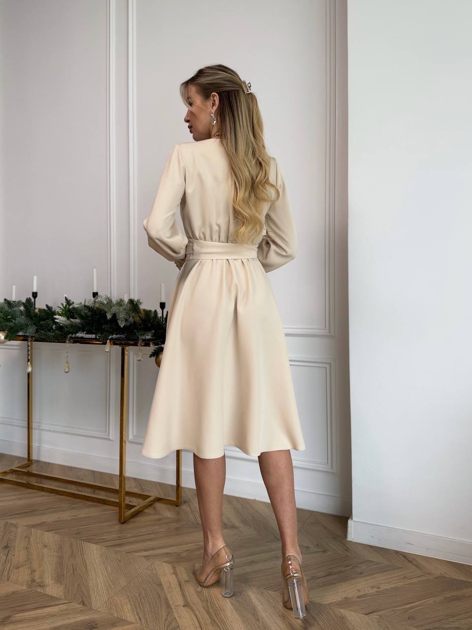 Woman in a beige dress standing in a room with a decorative table and candles.