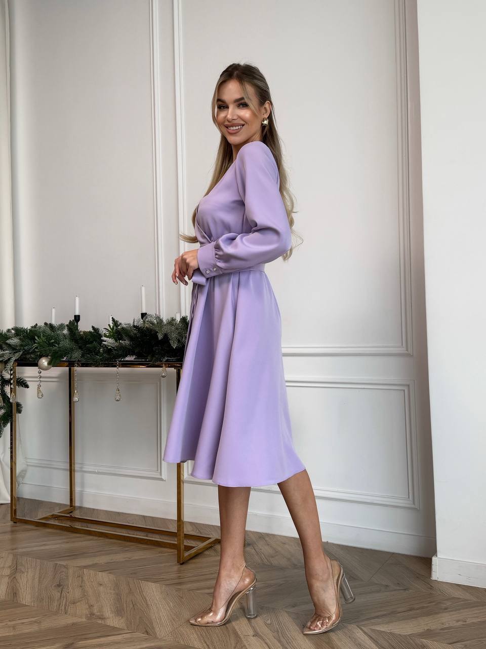 Woman wearing a light purple dress standing in a room with decorative elements.
