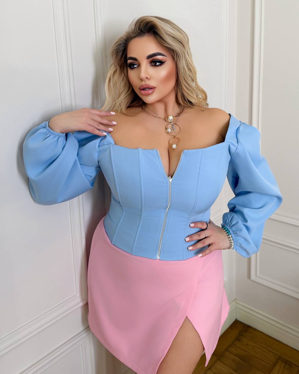 Woman wearing a blue and pink dress with puffed sleeves against a white wall.