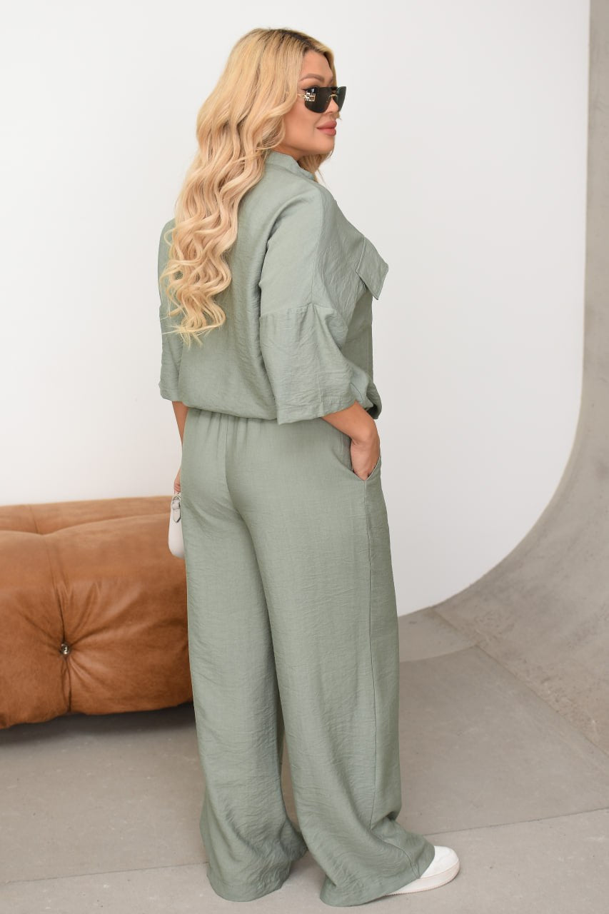 Woman wearing a green outfit standing against a white wall with a brown couch.