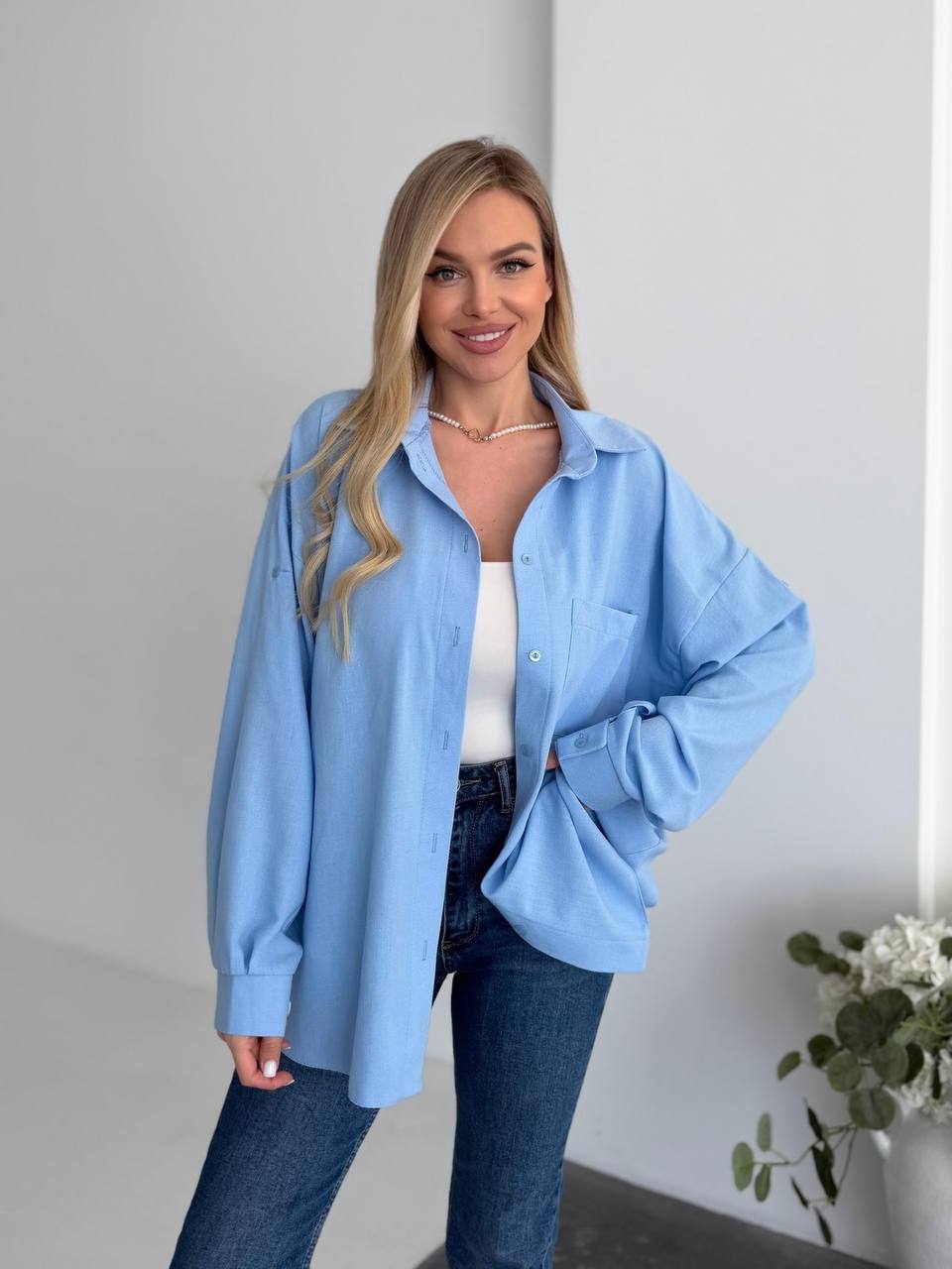 Woman wearing a light blue shirt and dark jeans against a plain background