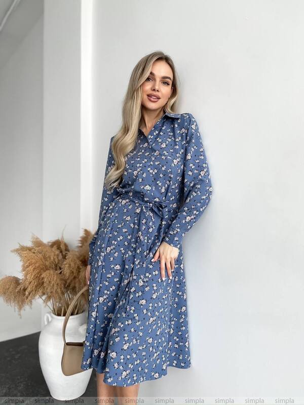 Woman wearing a blue floral dress against a white wall