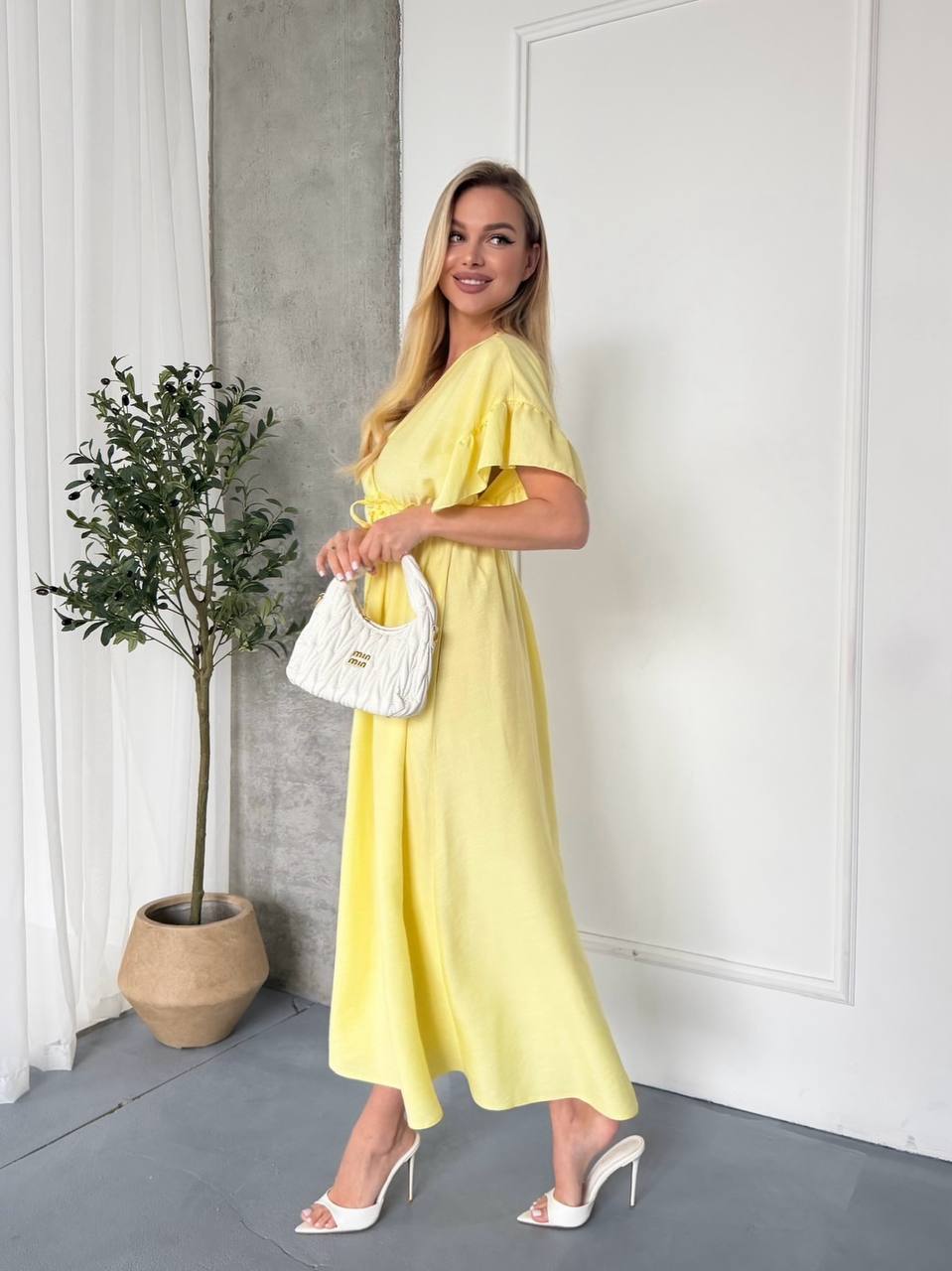Woman in a yellow dress holding a white handbag indoors.