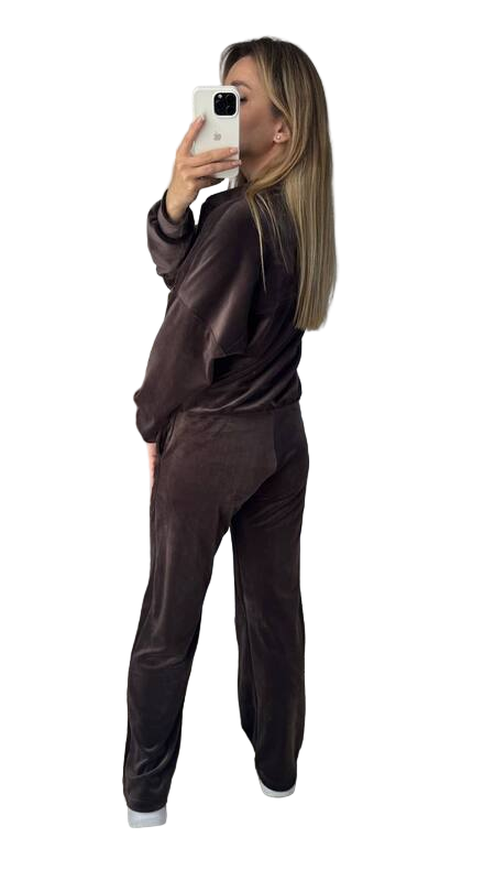Person wearing a brown velour tracksuit taking a selfie on a white background