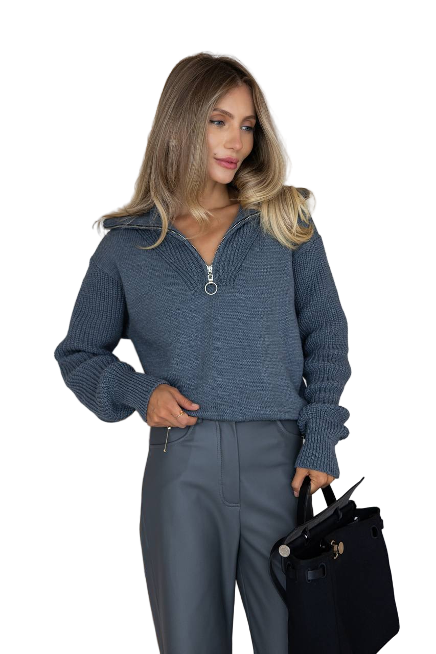 Woman wearing a blue sweater and pants holding a black handbag on a white background