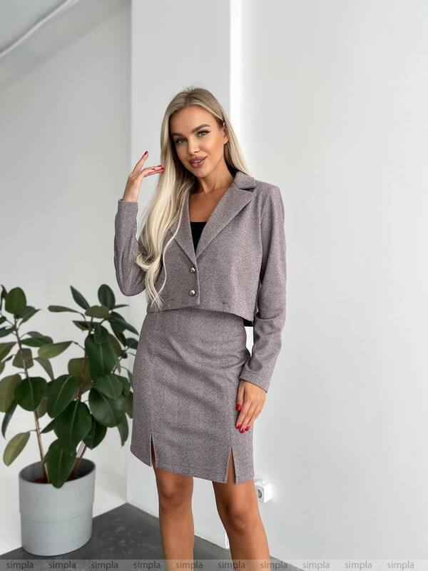 Woman wearing a gray suit with a plant in the background