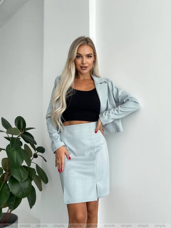 Woman wearing a light blue jacket and skirt with a black top indoors.