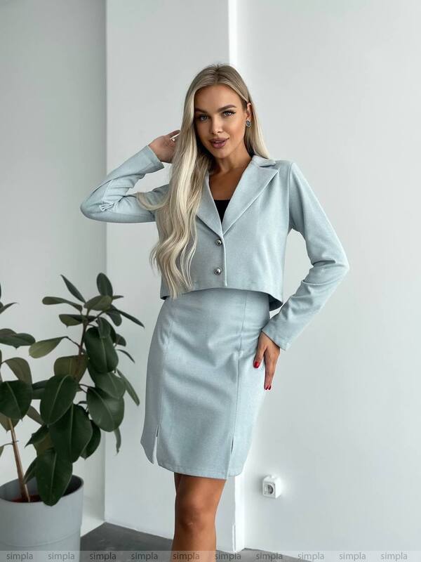 Woman wearing a light blue outfit standing in a room with a plant.