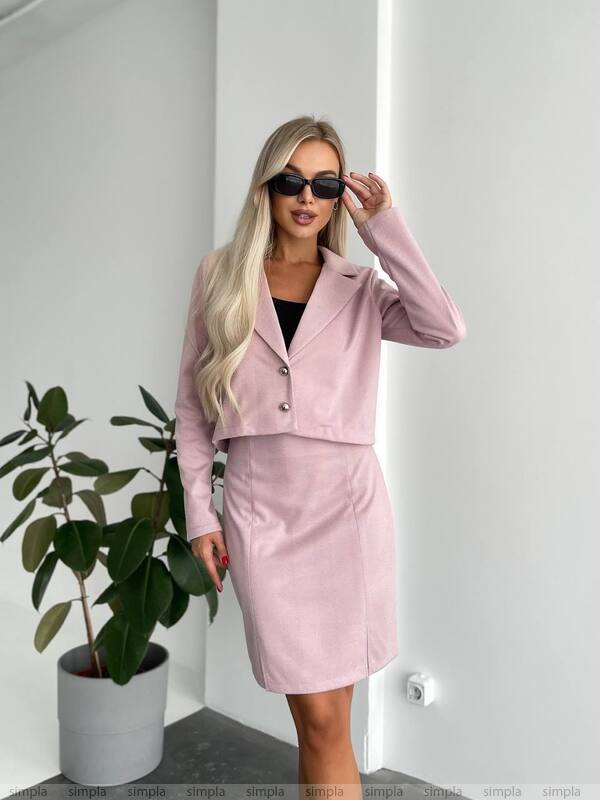 Woman wearing a pink outfit with sunglasses indoors next to a plant.
