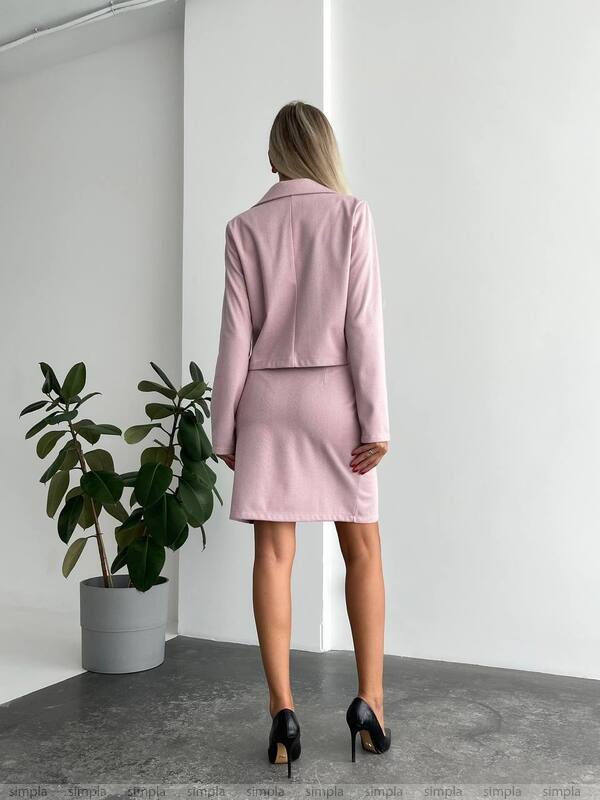 Woman in a pink suit standing in a minimalistic room with a plant.