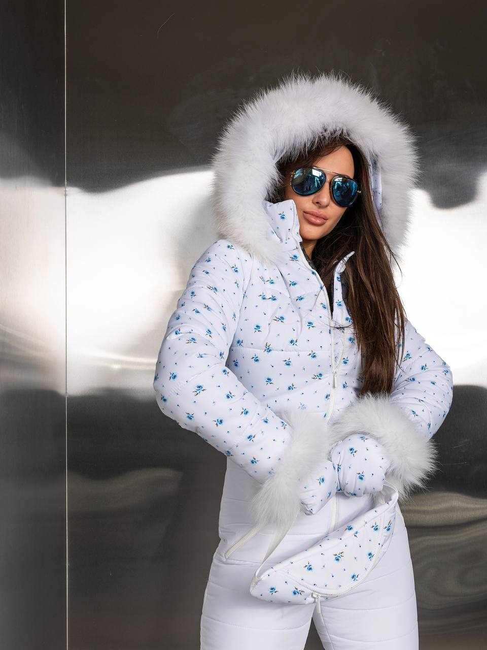 Woman wearing a white winter coat with fur hood and mittens in a snowy setting