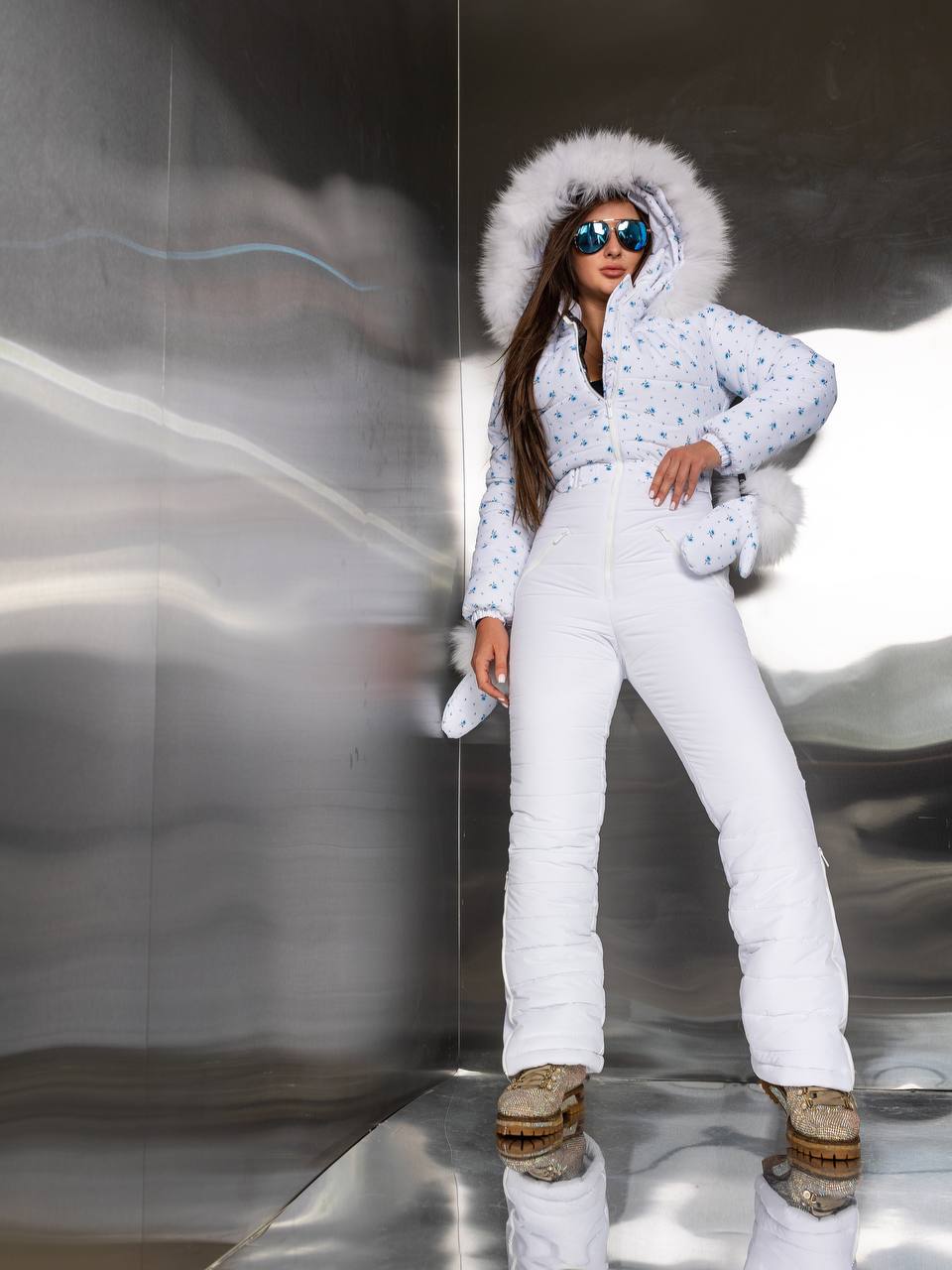 Person wearing a white snowsuit with a fur-lined hood in an indoor setting.
