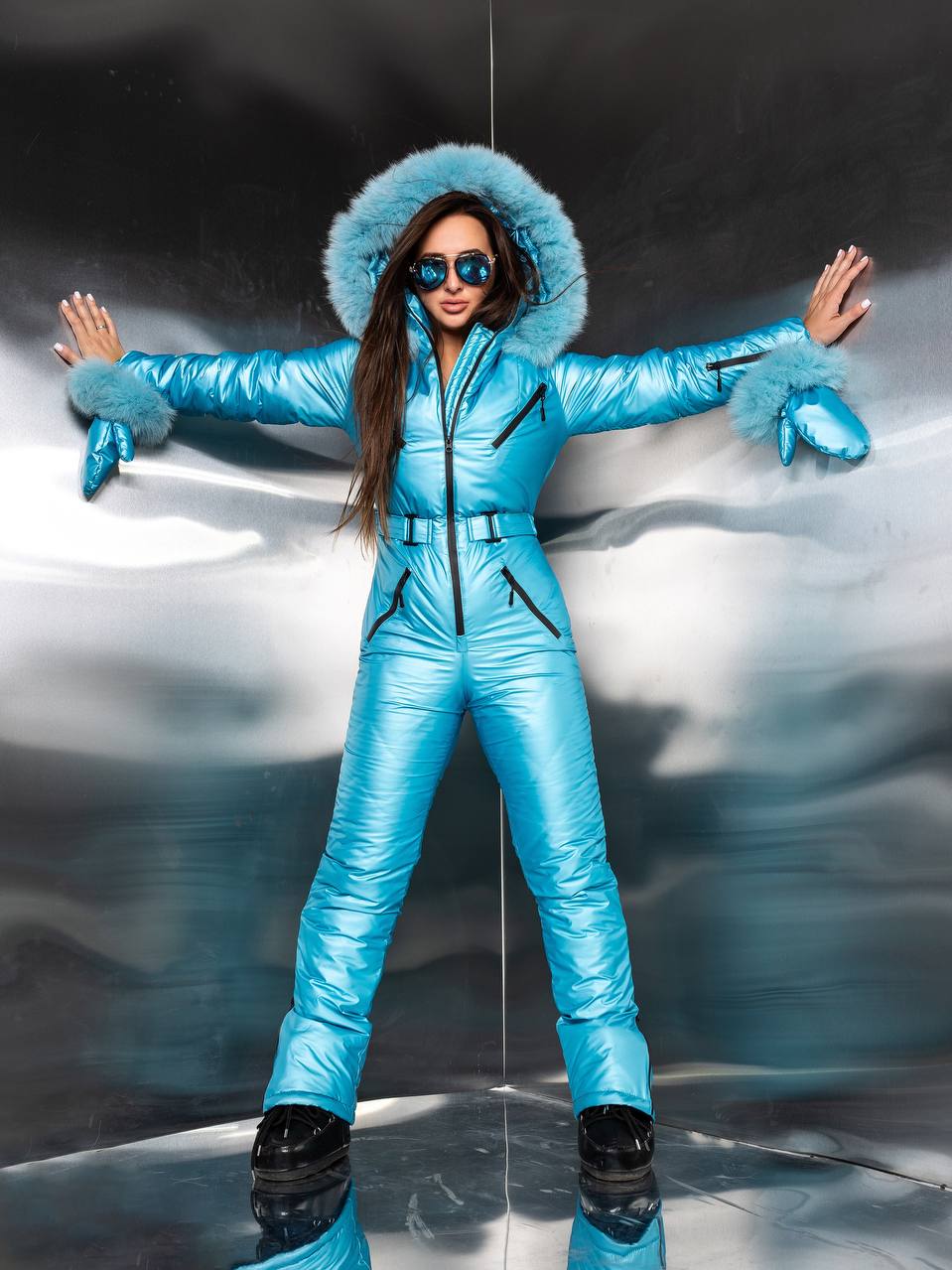 Person wearing a blue puffer suit with fur-lined hood against a reflective surface.