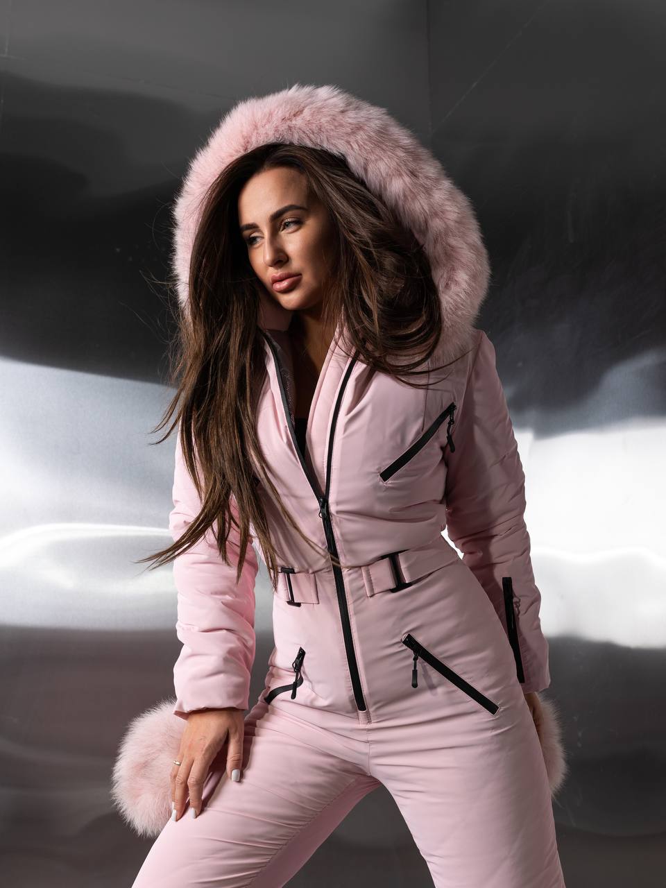 Woman wearing a pink snowsuit with a fur-lined hood against a snowy background