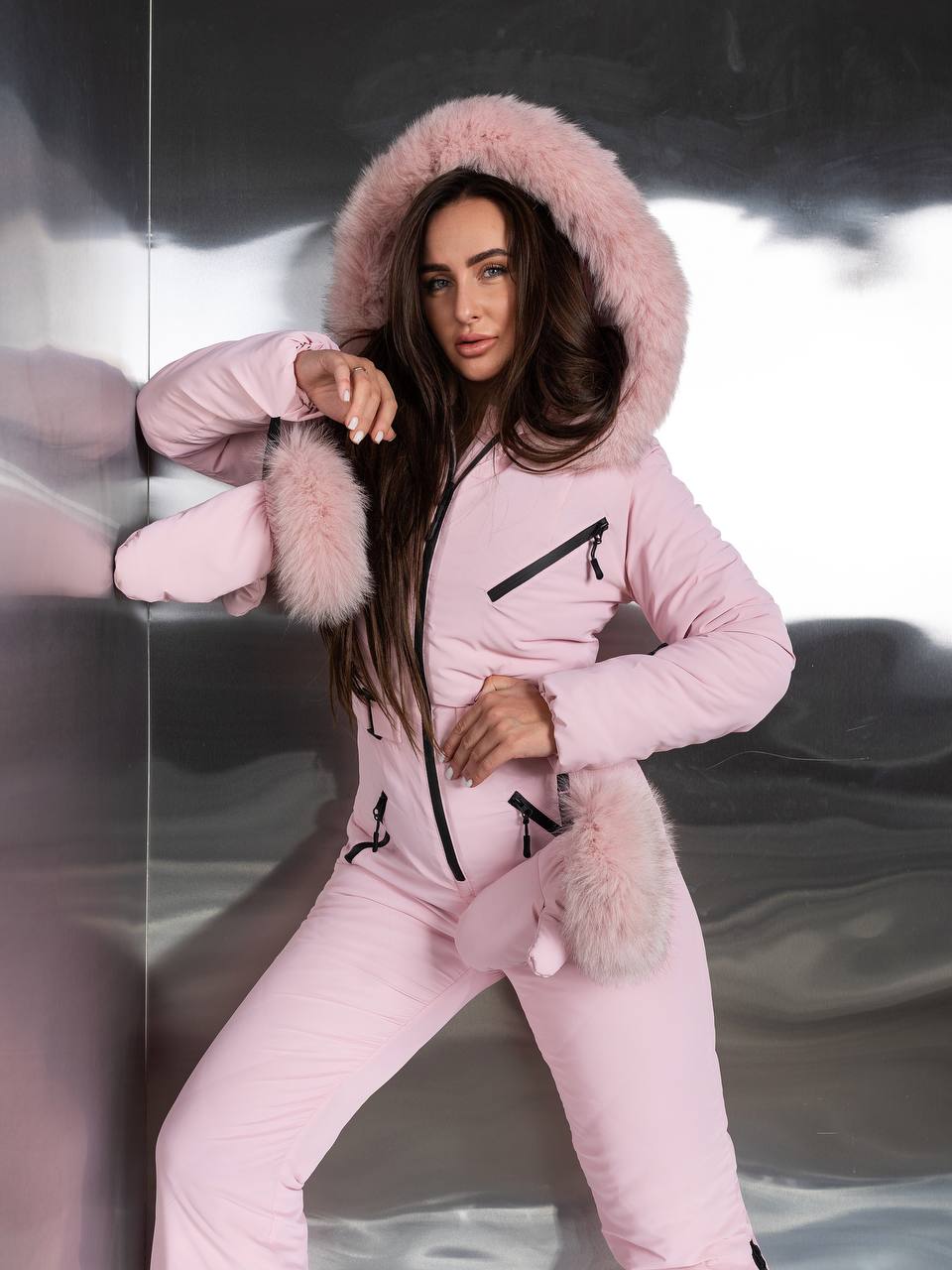 Woman wearing a pink onesie with fur trim against a reflective surface.