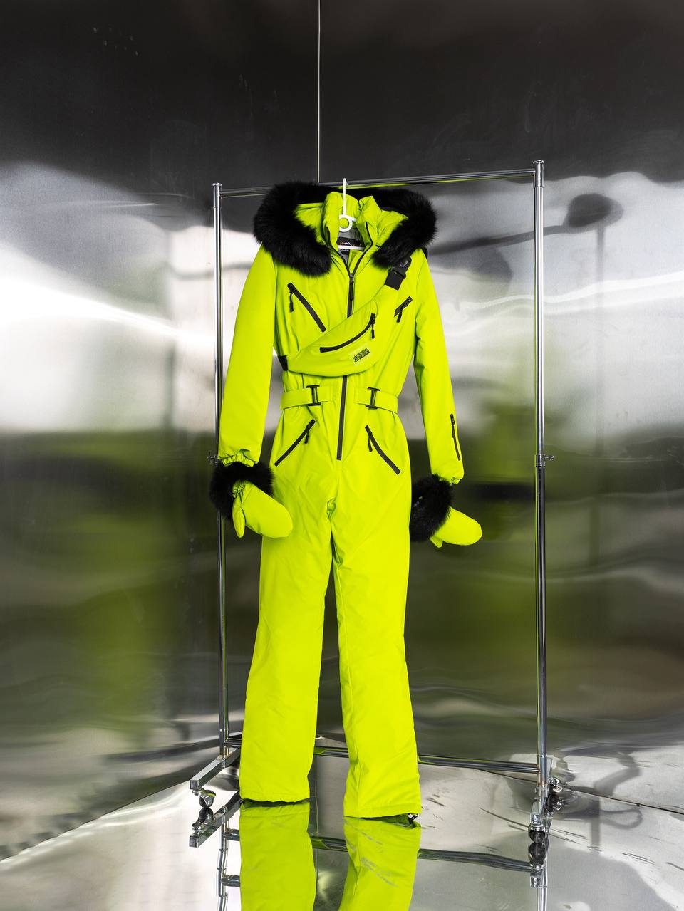 Bright yellow ski suit with black fur trim on a mannequin against a reflective surface.