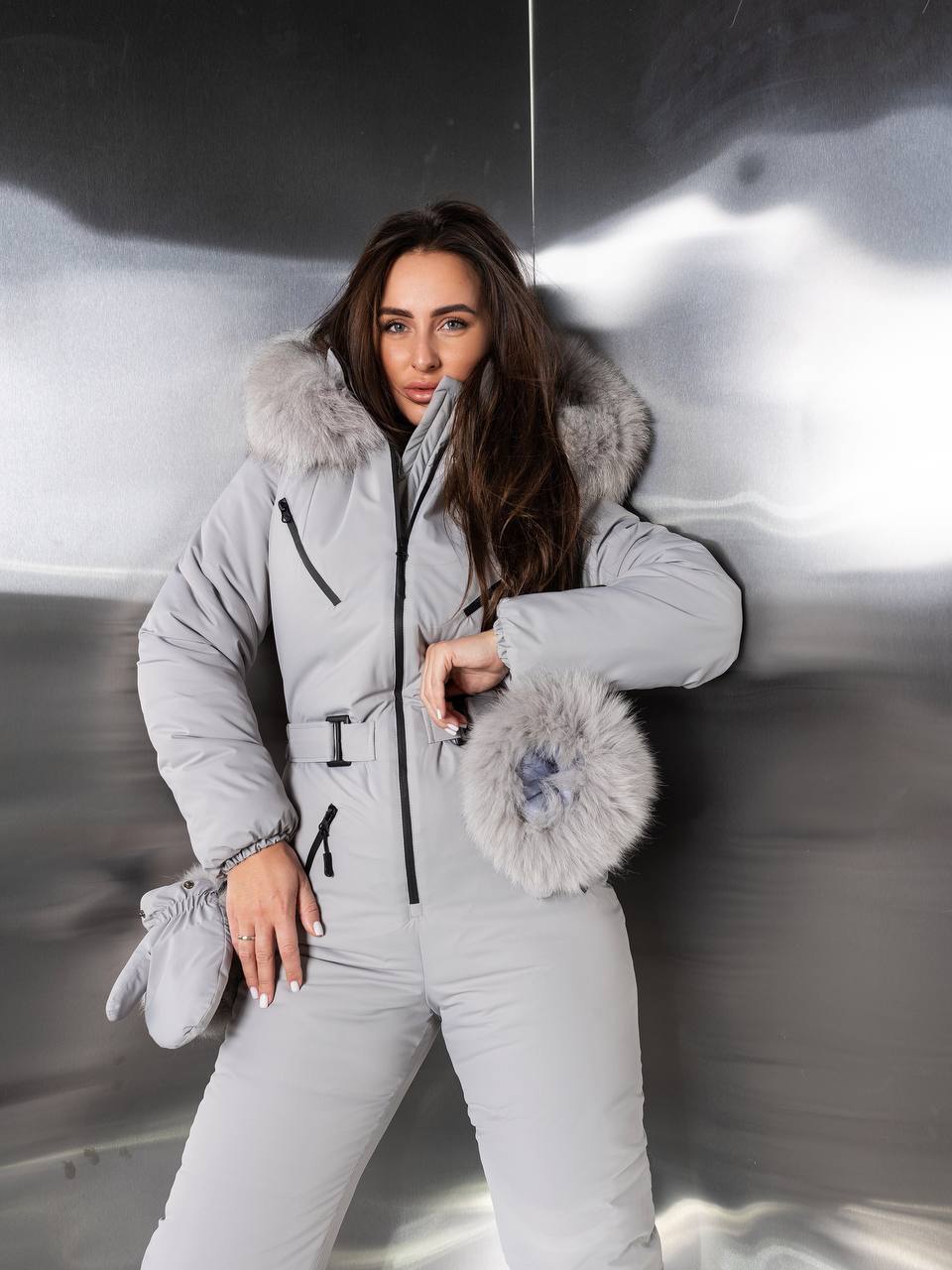Woman wearing a gray snowsuit with fur trim against a reflective surface.