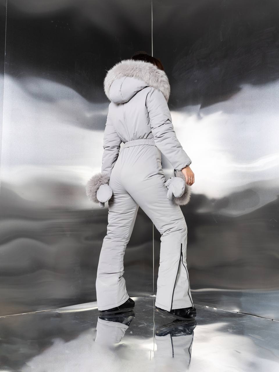 Person wearing a gray puffer suit with fur trim against a reflective surface.