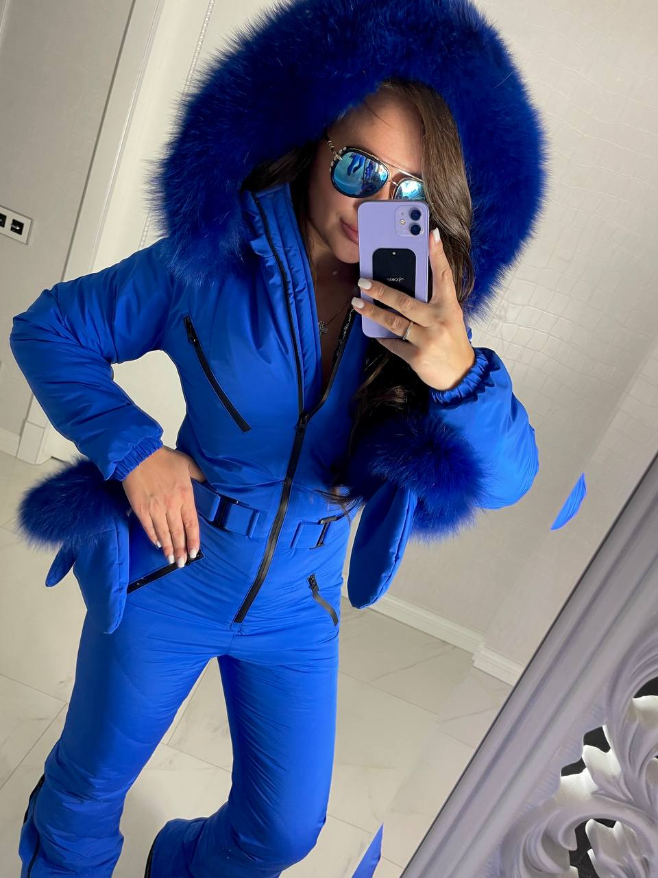 Person wearing a blue snowsuit with a fur-lined hood taking a mirror selfie.