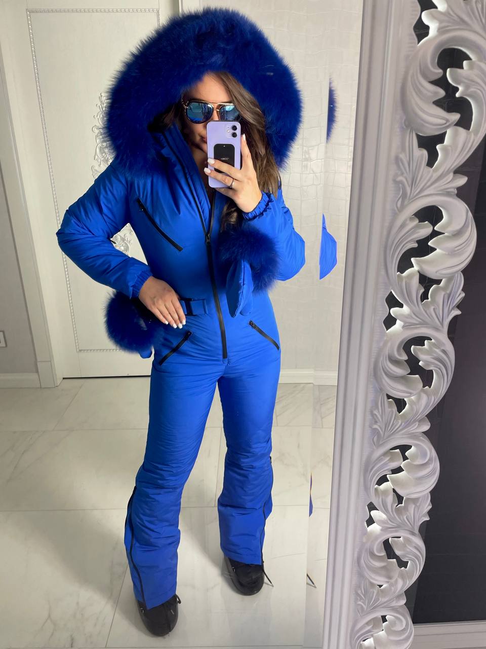 Person wearing a blue snowsuit with a fur-lined hood in front of a mirror.