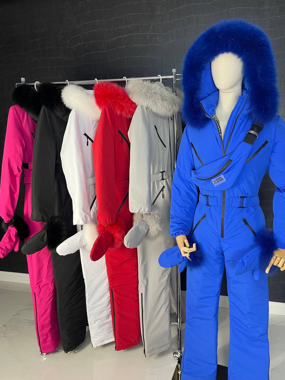 Blue snowsuit with fur hood on a mannequin in front of other colorful snowsuits.