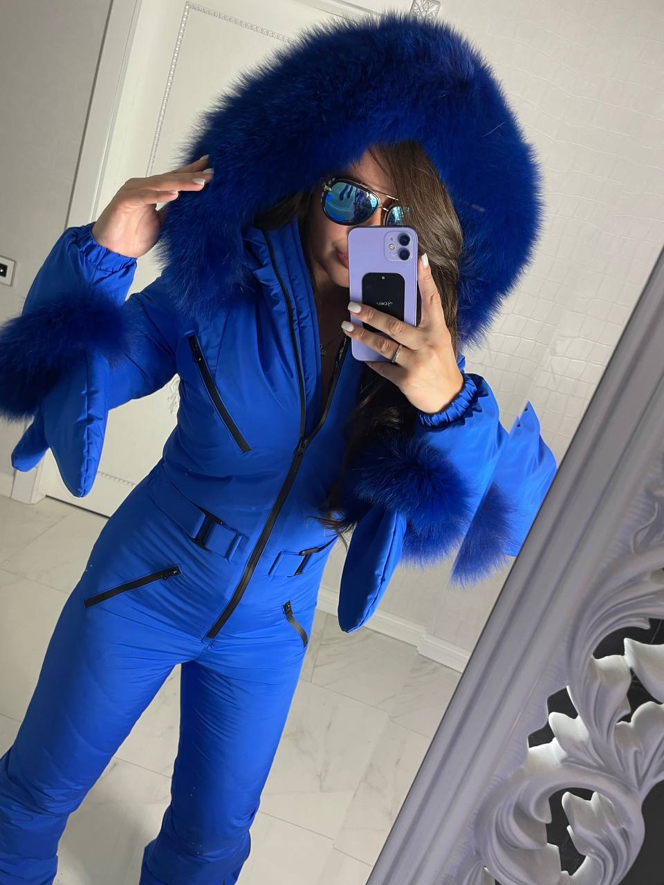 Person wearing a blue snowsuit with a fur-lined hood taking a mirror selfie.