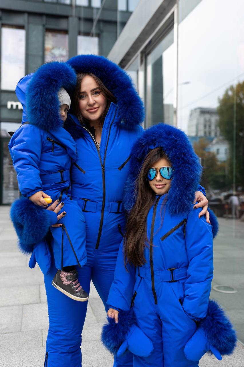 Two women and a child wearing matching blue fur-lined coats in an urban setting.