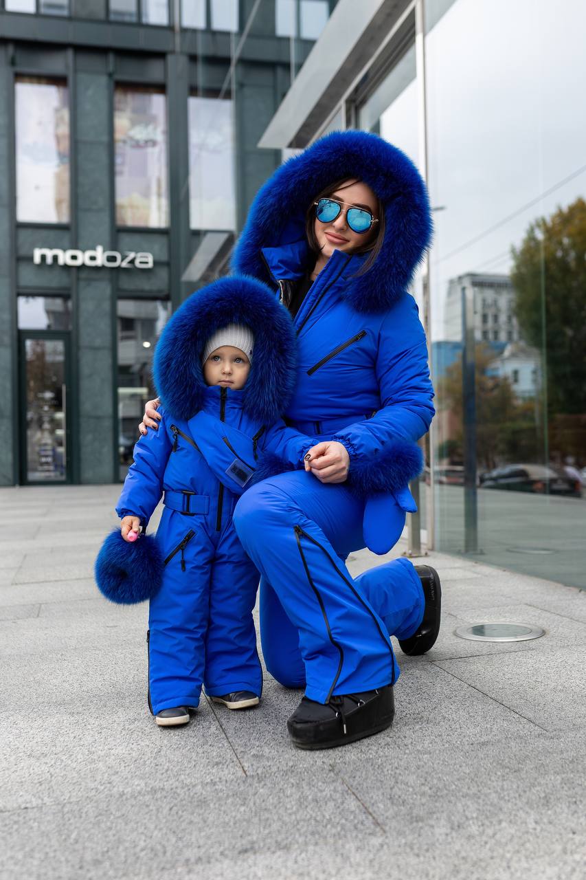 Woman and child in matching blue snowsuits standing on a city street.