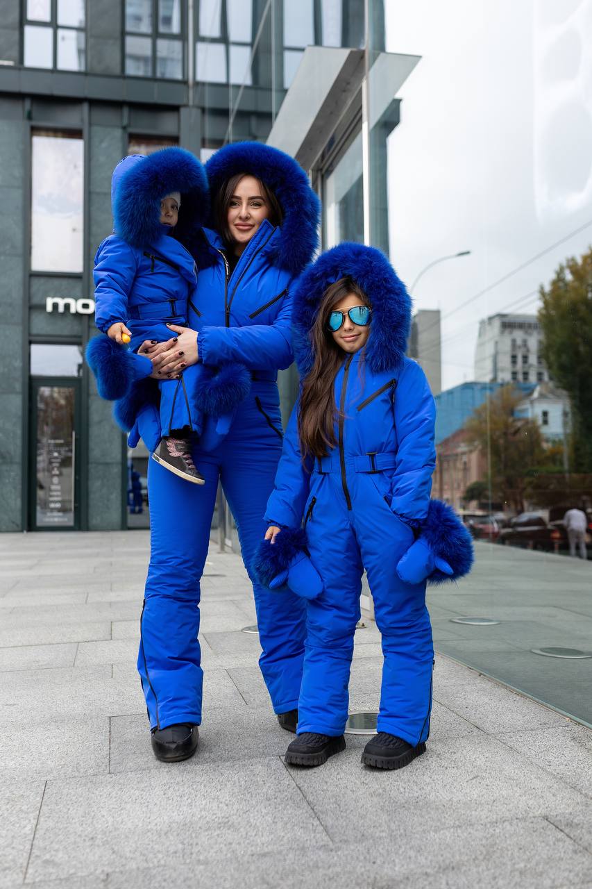 Two women and a child in matching blue snowsuits on a city street.