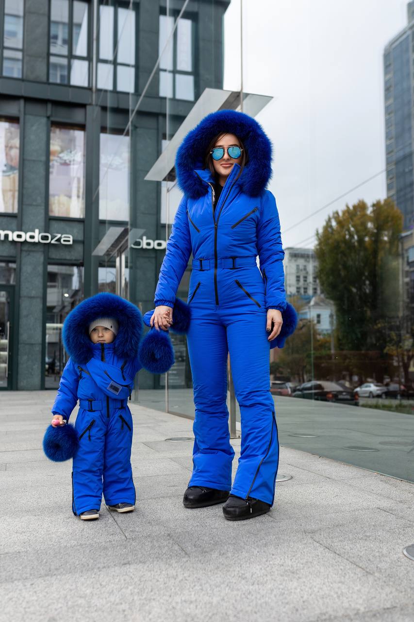 Two people in matching blue snow suits standing on a city street.