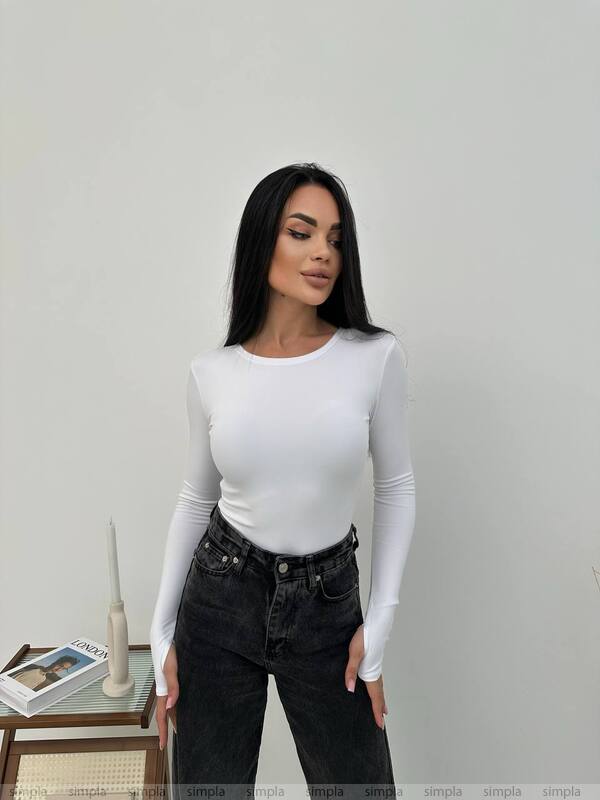 Woman wearing a white long-sleeve top and black jeans against a plain background