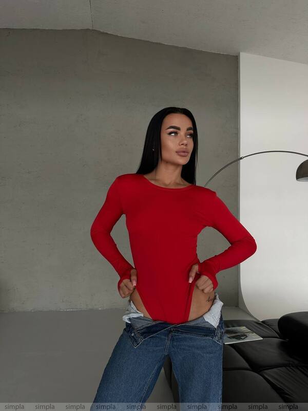 Person wearing a red long-sleeve top and blue jeans in an indoor setting