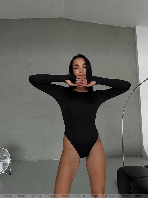 Person wearing a black bodysuit in a minimalistic room.