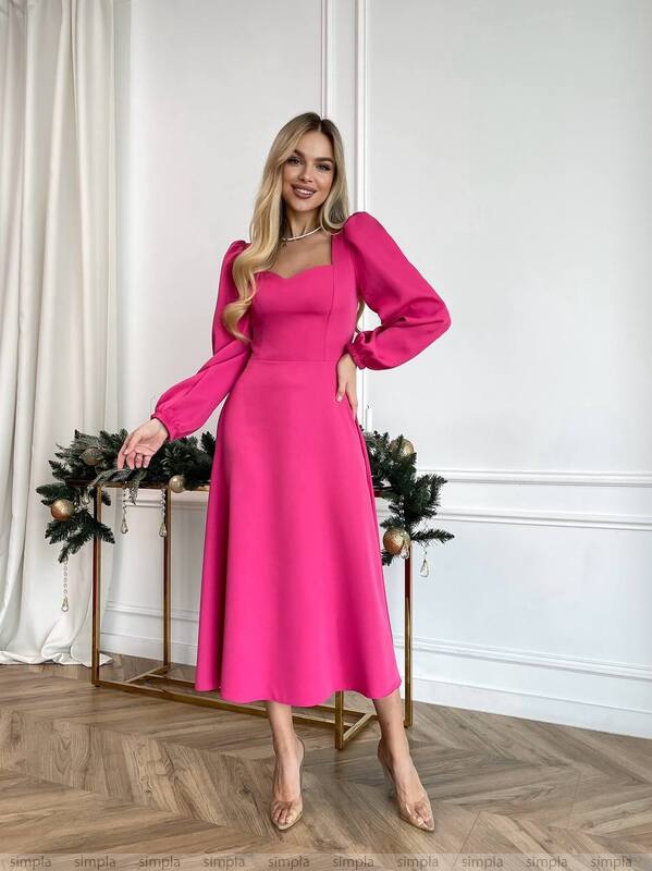 Woman wearing a bright pink dress standing in a room with white walls and wooden floor.