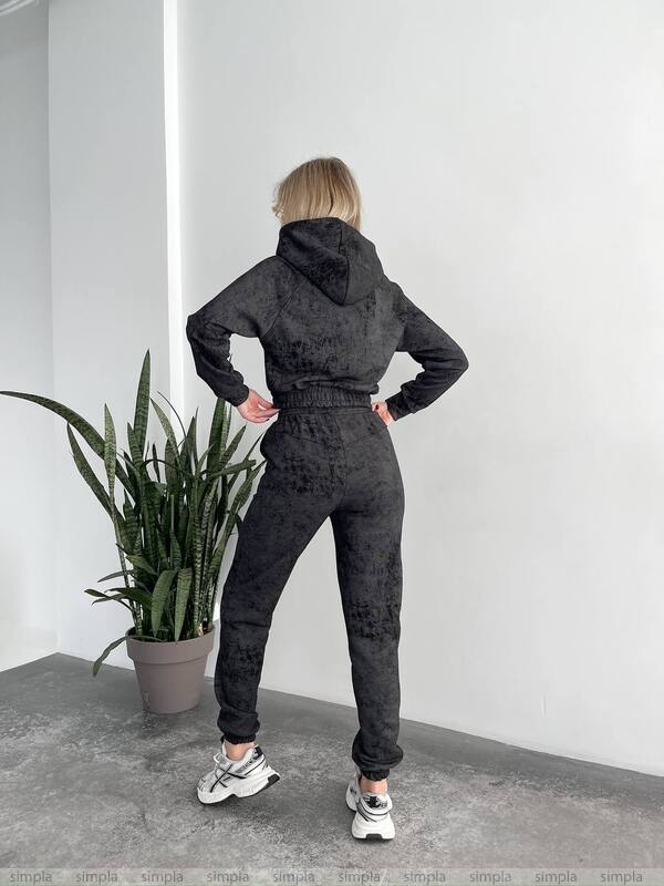 Person wearing a dark gray tracksuit standing in a room with a plant.