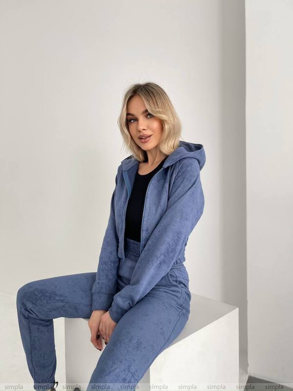 Woman wearing a blue tracksuit sitting on a white surface with a plain background