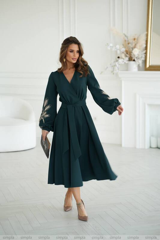 Woman in a dark green dress standing in a bright room with white walls and decor.